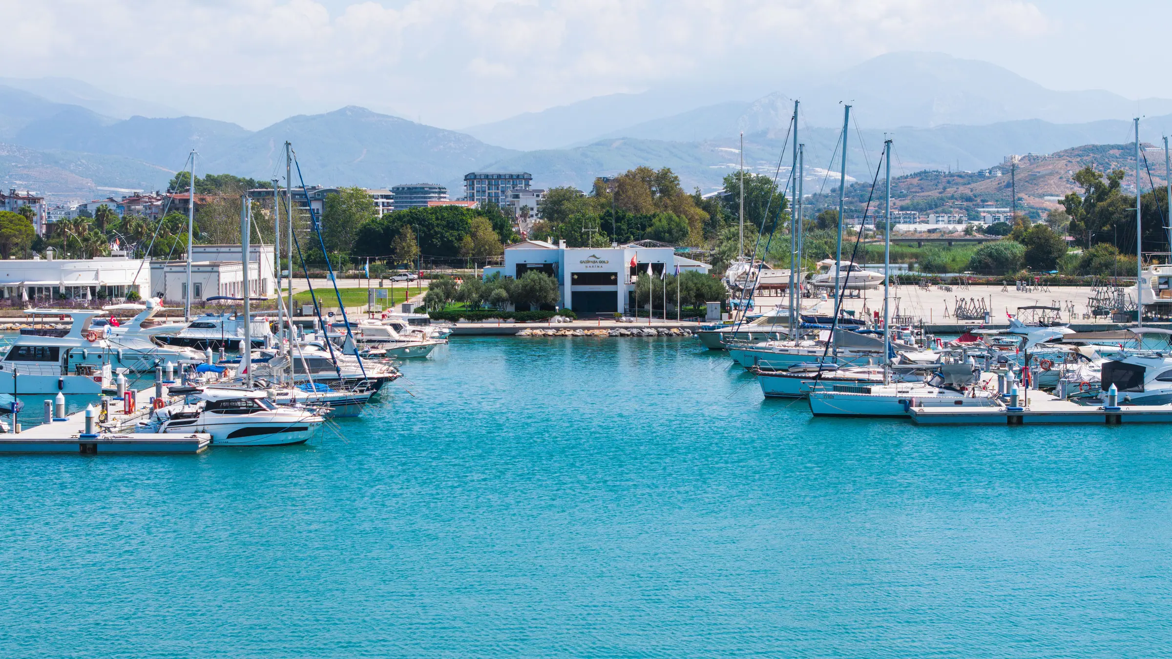 Yachts moored at the pontoons of Gazipaşa Gold Marina, with the marina building and the Taurus Mountains behind